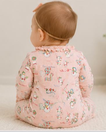 Baby in a pink floral outfit sitting on a light surface with a neutral background