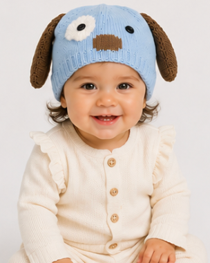 Baby wearing a blue knitted hat with dog ears and a cream outfit on a white background