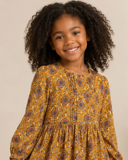 Young girl wearing a yellow patterned dress with brown boots against a neutral background