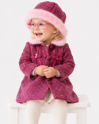 Child wearing a pink coat and hat sitting on a white stool against a white background