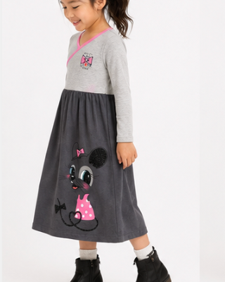 A young girl with a high ponytail is wearing a long-sleeve colorblock dress with a gray top, a dark gray skirt featuring a Minnie Mouse graphic, and black ankle boots. She is standing against a plain white studio background.