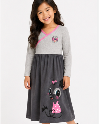 A young girl modeling a long-sleeve dress with a light gray v-neck bodice, dark gray skirt, and a cartoon cat graphic on the front, set against a plain white studio background.