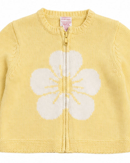 A yellow knit zip-up cardigan sweater for babies, featuring a large white flower motif knitted onto the front.
