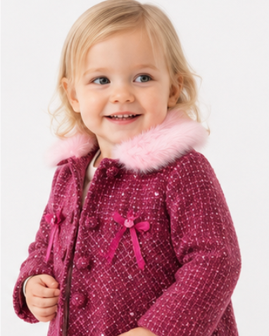 Child wearing a pink coat with a bow and fur trim on a white background