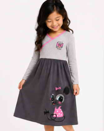 A young girl modeling a two-tone dress with a light gray long-sleeve top and a dark gray skirt featuring a cartoon dog graphic. The dress has a pink crossover neckline and a pink polka-dot bow on the skirt.